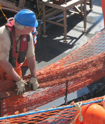 Worker handling commercial fishing net on deck