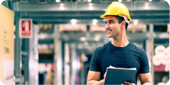 Engineer in a hard hat reviewing inventory with a clipboard in a warehouse